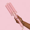 Pink hair curler held by a hand against a pink background