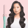 Woman with styled hair holding a teal and pink hair straightener against a pink background