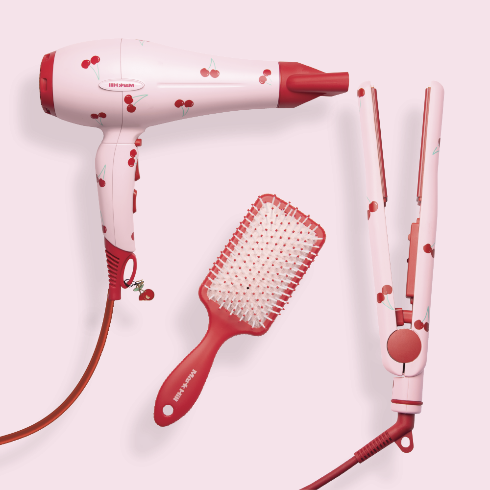 A set of hair styling tools including a hair dryer, straightener, and paddle brush, all with a cherry print design in red and white.
